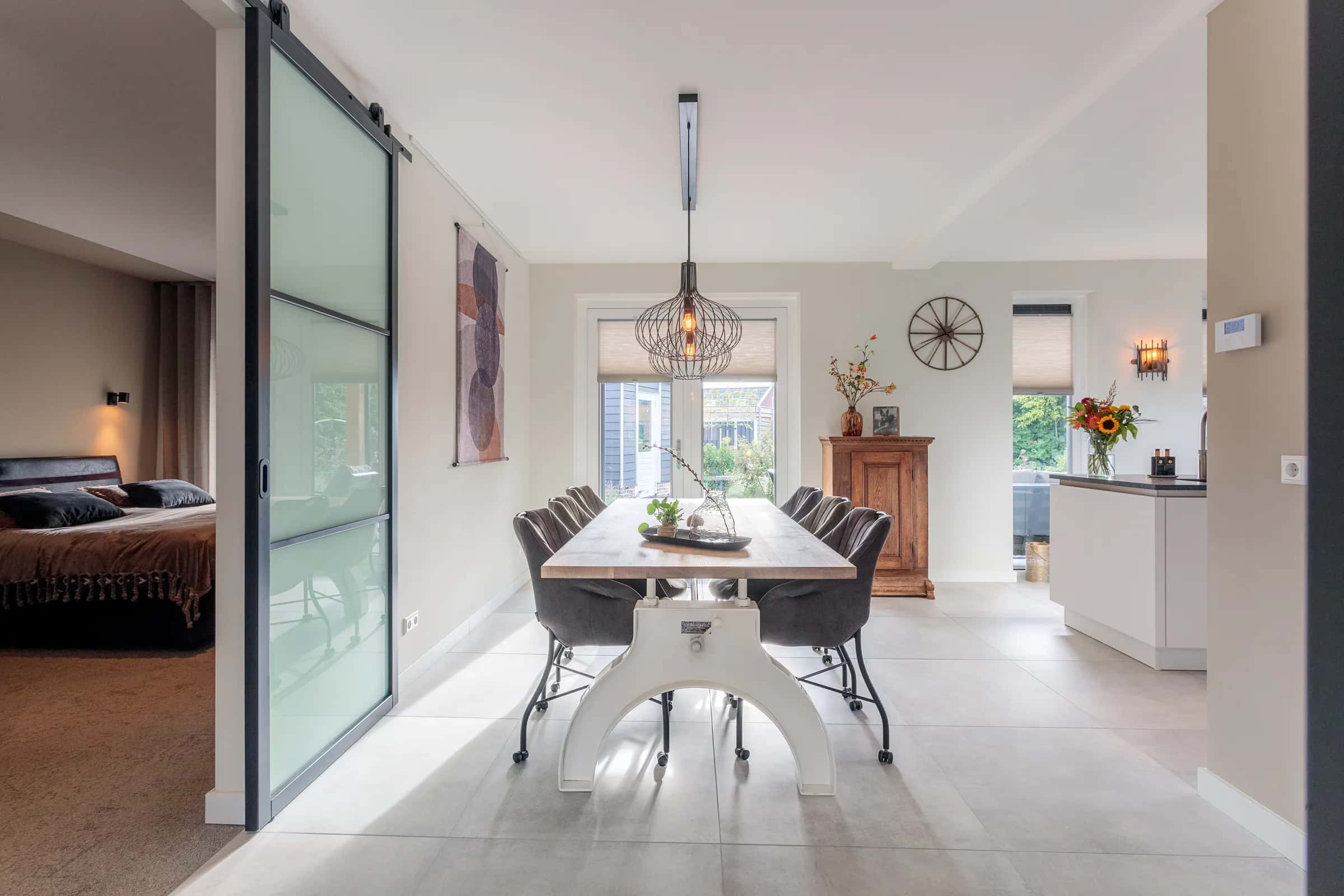 Handcrafted industrial dining table with an oak top on a white cast base with a handwheel, grey chairs and a pendant lamp in a bright home