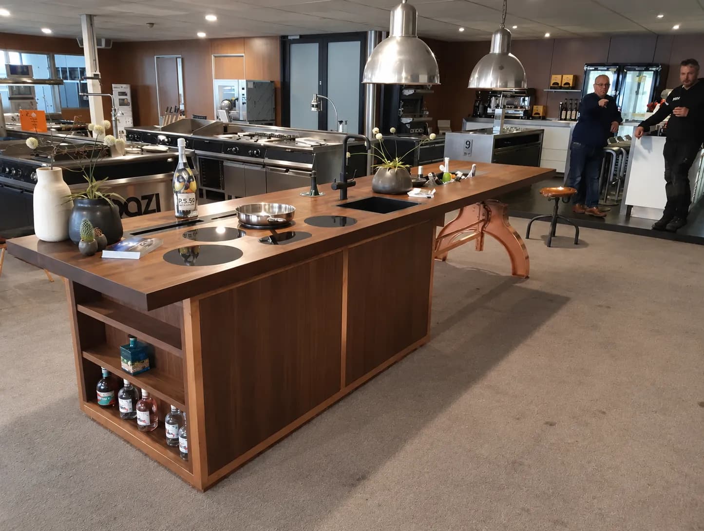 Walnut kitchen island on a copper coloured cast base in a showroom kitchen with steel pendant lamps