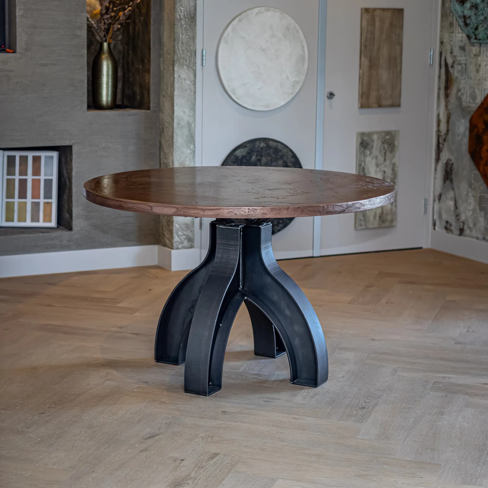 Round table with a copper coloured top on a black double arch base on a herringbone floor
