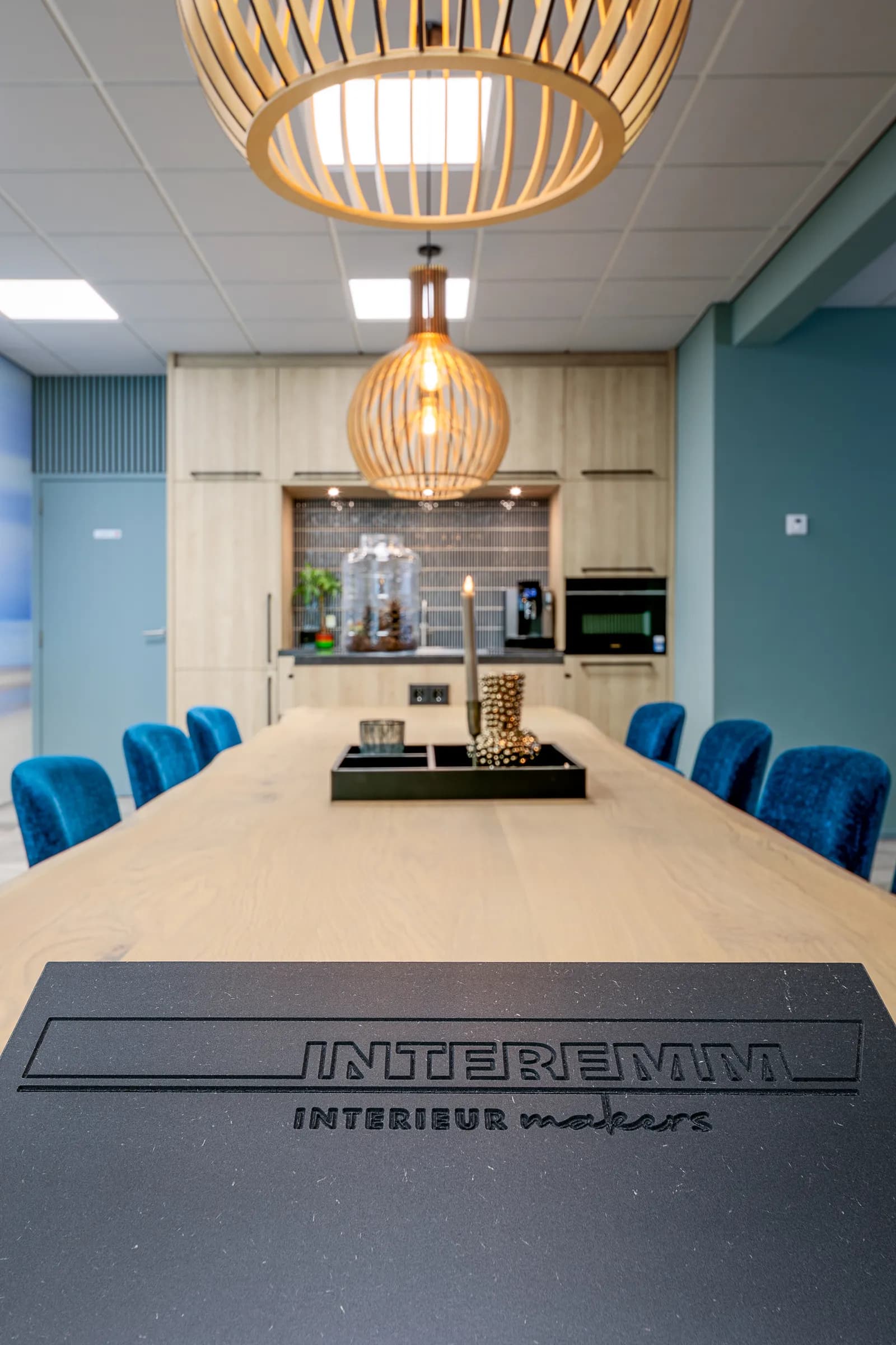 Long oak table with blue velvet chairs and wooden pendant lamps, the client name milled into the black base