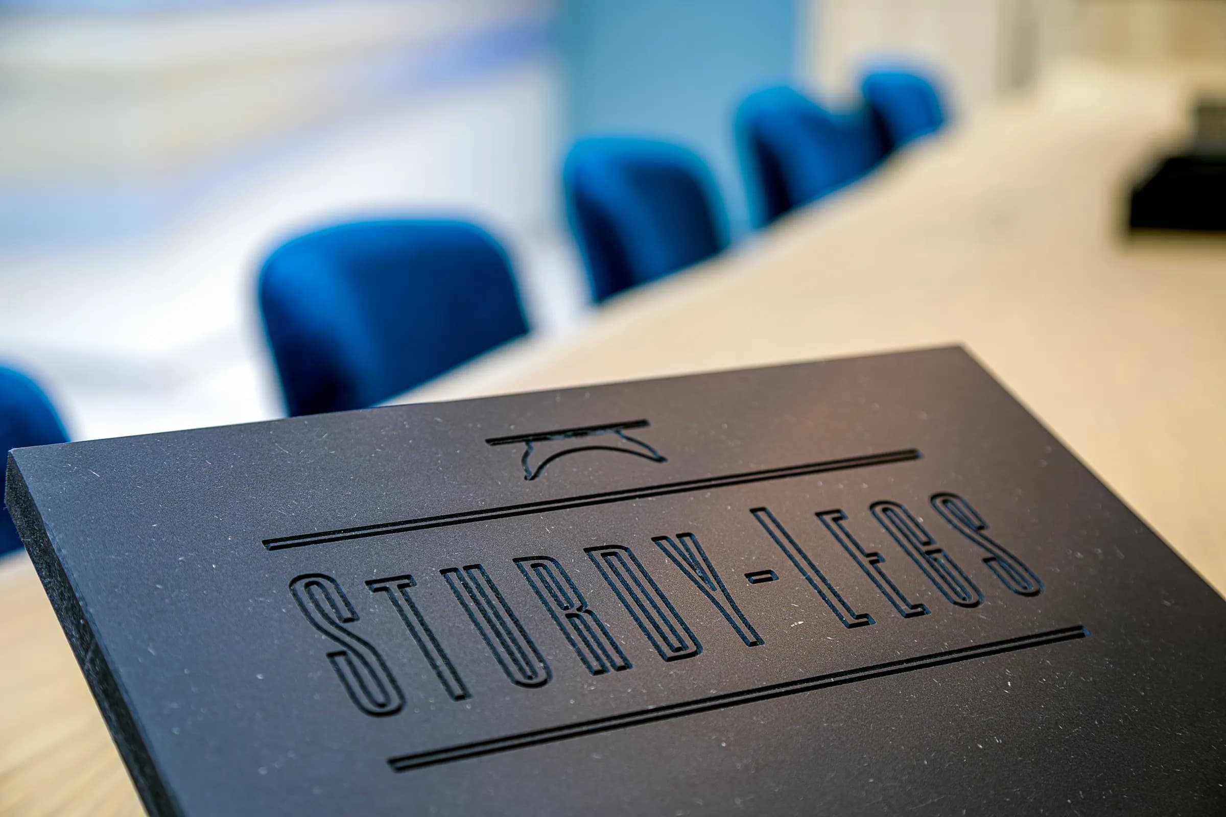 Close-up of the black steel table base with the Sturdy-Legs logo milled in, blue chairs behind