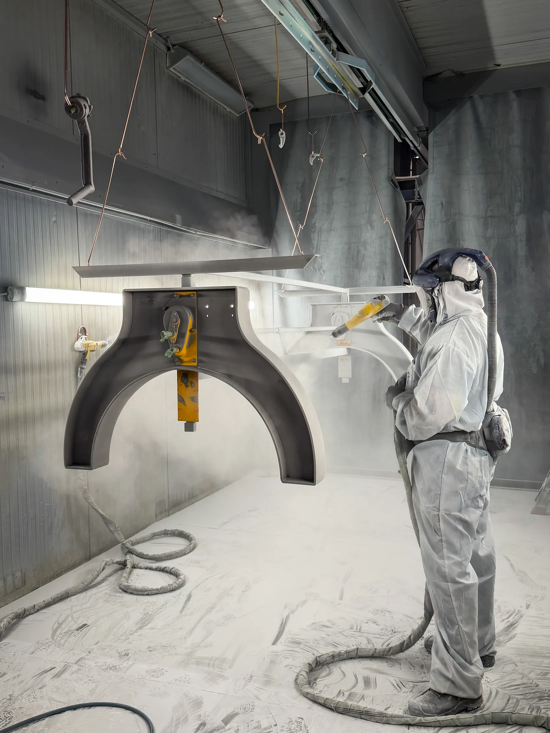 Steel table base being coated by a worker in protective clothing in the workshop