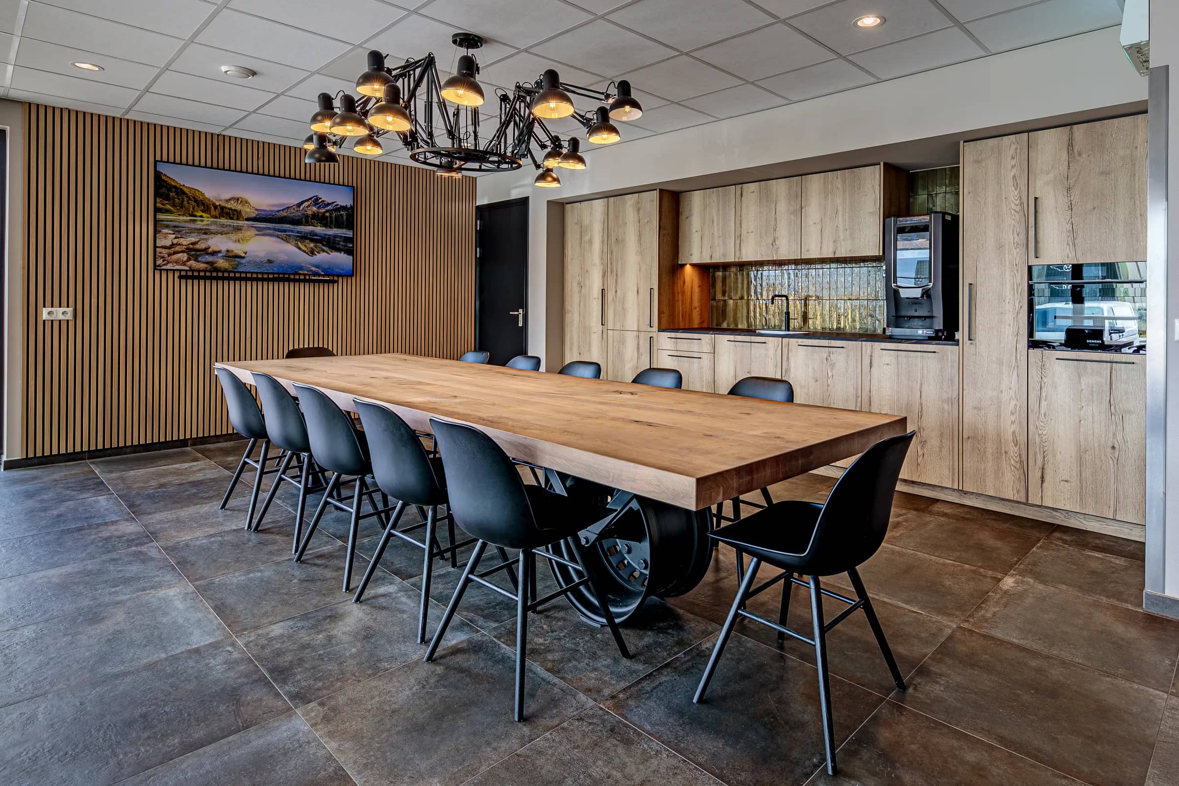 Canteen with a long light table on a car rim base, black chairs and a wooden slat wall at Van Wieren in Emmeloord