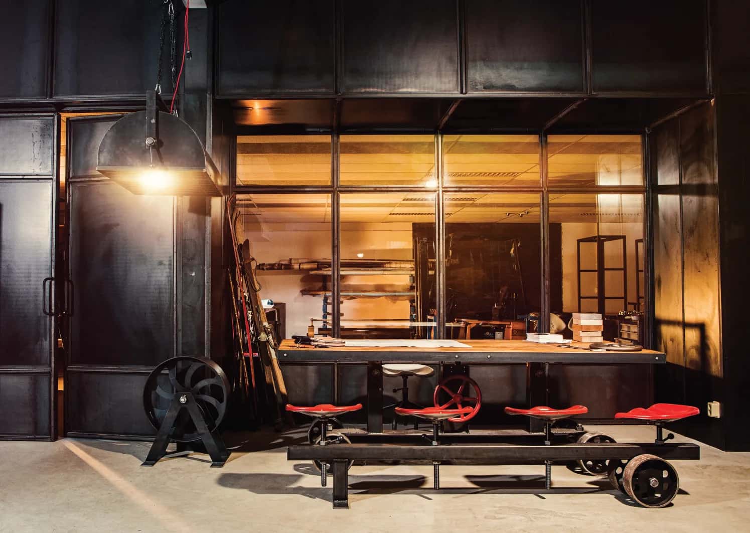 Long bistro bar on a wheeled steel frame with red bar stools in a dark steel clad showroom