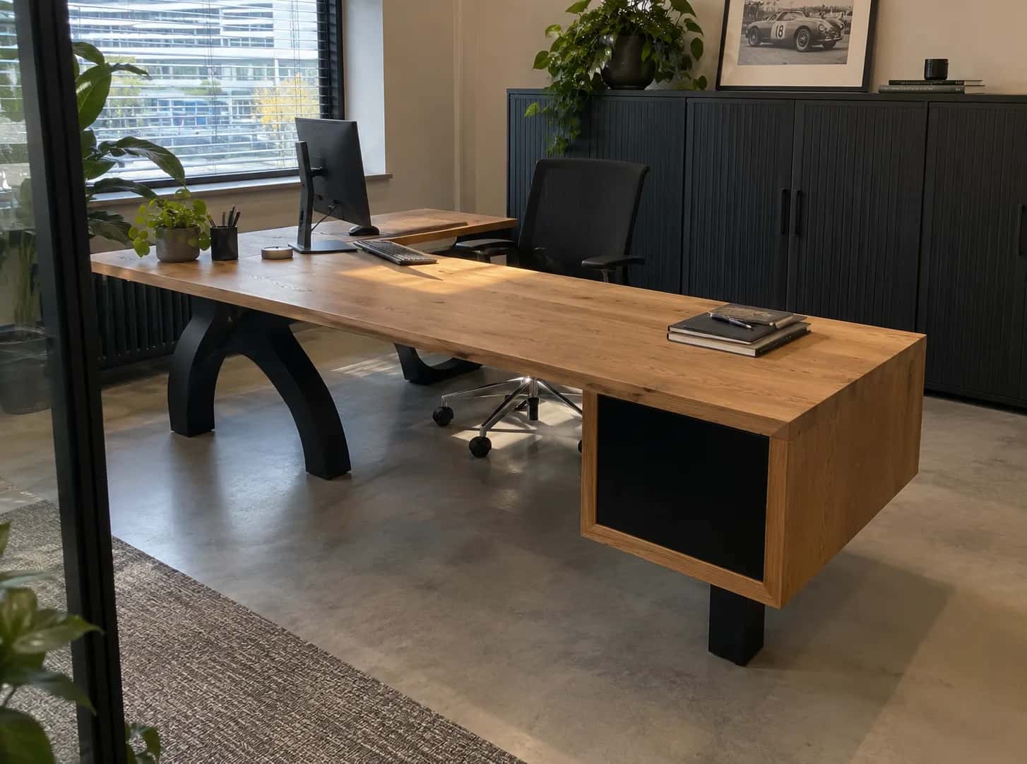 Oak desk on a black arched cast base with a matching cabinet, an office chair and plants