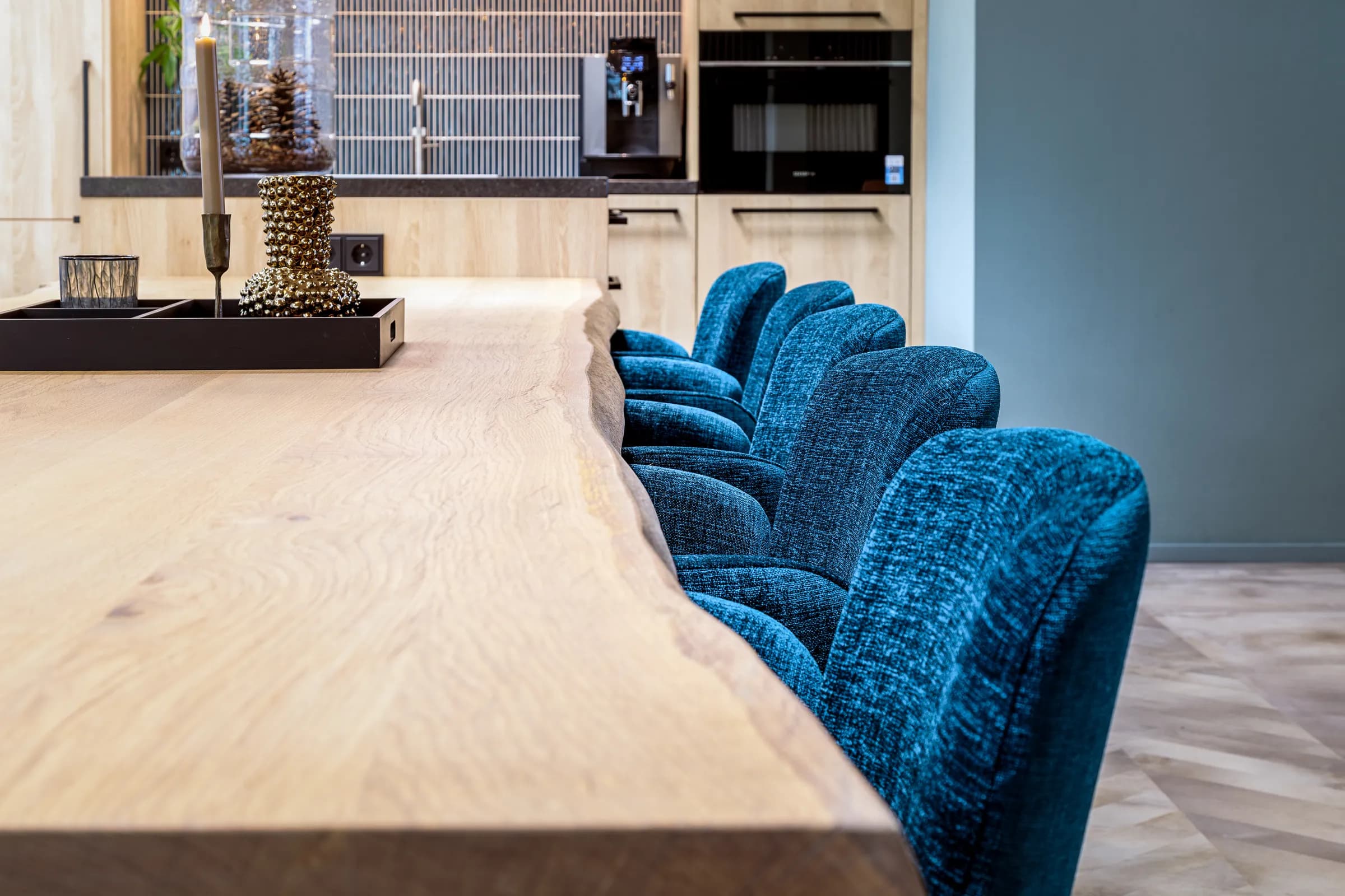 Solid oak table top with a natural live edge and blue velvet chairs in a modern kitchen