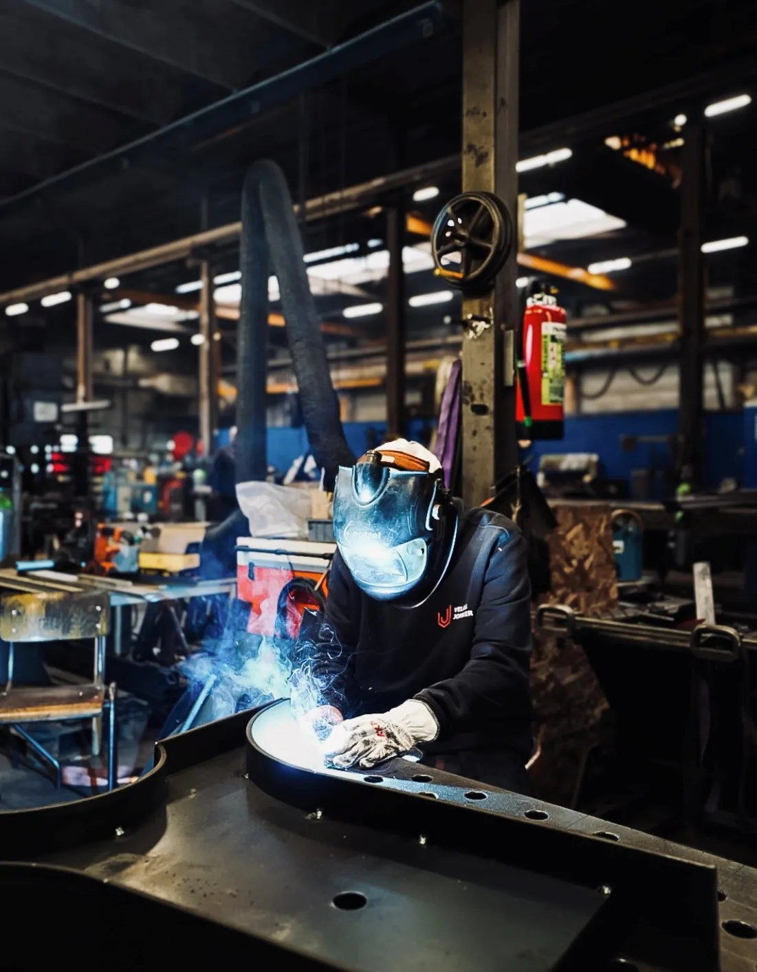 Welder in a mask joining a curved steel table frame in the Sturdy Legs workshop